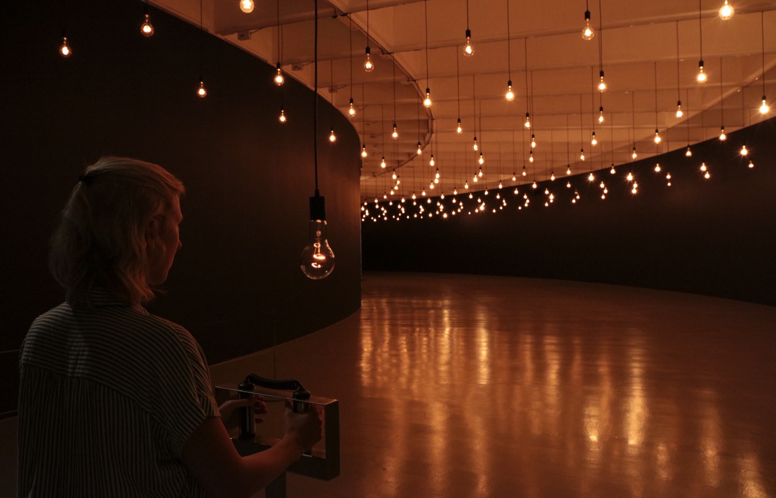 A visitor holds a heart-rate sensor beneath a grid of glowing bulbs in Rafael Lozano-Hemmer's Pulse Room